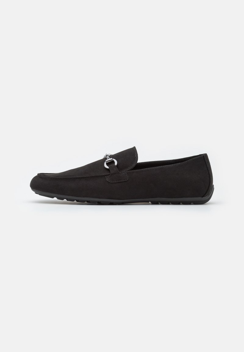 Mocassin en daim noir avec détail en métal argenté, bout arrondi et semelle en caoutchouc, vu de côté sur un fond uni.