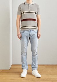 Camisa polo de punto gris con un diseño acanalado, que presenta rayas horizontales en rojo, negro y crema, combinada con jeans azul claro y zapatillas blancas.