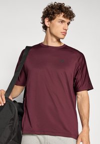 Bordeaux T-shirt met korte mouwen en een ronde hals, gemaakt van een soepel stof; heeft een klein zwart logo op de borst en een relaxed fit.