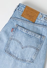 Ανοιχτό μπλε τζιν παντελόνι Levi's που δείχνει την πίσω τσέπη, ραμμένο σχέδιο τόξου, κόκκινη ετικέτα Levi's και καφέ δερμάτινη ετικέτα της μάρκας Levi Strauss & Co.