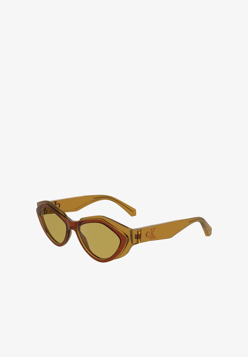 Óculos de sol de plástico castanho e âmbar com um formato angular de gato, lentes amarelas e uma marcação subtil na haste. As armações transparentes realçam o design.