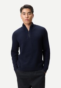 Marinblå zip-neck tröja med ett strukturerat mönster och ribbad krage. Tyget är mjukt och stickat, med långa ärmar och avslappnad passform.