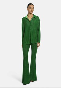 Groen metallic tweedelig outfit bestaande uit een lange mouwen overhemd met kraag en flared broek, beide met een glanzende textuur.