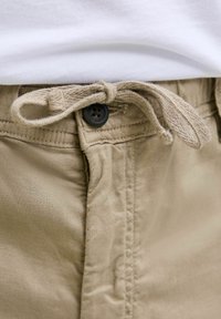 Khaki szorty z zapięciem na sznurek, z czarnym guzikiem, gładkim bawełnianym materiałem i widocznymi detalami szwów.