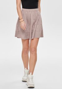 Světle růžová sukně ke kolenům vyrobená z měkké semišové tkaniny, s elastickým pasem a vrstveným designem. Spárována s bílými teniskami.