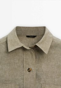 Beige linned skjorte med krave, en enkelt knaplukning og en brystlomme. Teksturen er glat med en naturlig finish.