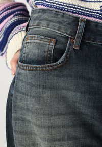 Mørkeblå denimjeans med oransje sømmer, som har en baklomme, lett bleket tekstur og en tettsittende passform rundt livet.