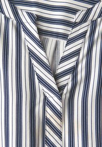 Blusa a righe blu navy e bianca con scollatura a V. Materiale liscio con motivi a strisce verticali e diagonal. Dettagli di cucitura sottili.