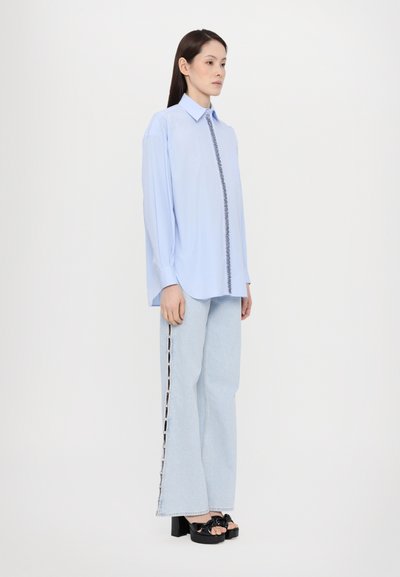 Light blue button-up shirt with a front seam detail, paired with light blue flared jeans featuring side cutouts, and black platform sandals.