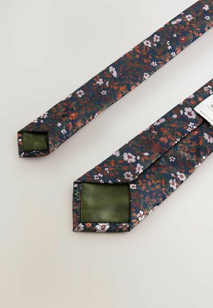 Florale Krawatte mit navy Hintergrund, verziert mit roten und weißen Blumen. Die Rückseite ist aus einfarbigem grünen Satin. Quadratische Enden und glatte Textur.