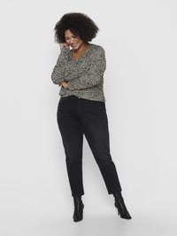 Blusa de mangas longas preta com um padrão floral, combinada com calças de ganga pretas de cintura alta e botins pretos. A modelo está em uma pose relaxada.