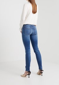 Blå skinny jeans med hög midja, ljus blekning och femfickorsdesign, i kombination med en krämfärgad långärmad topp och beige klackar.