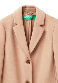 Beige kabát z vlněné směsi s klopovým límcem, dvěma hnědými knoflíkovými zapínáními a hladkou podšívkou se štítkem.