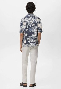 Camicia a maniche corte, blu navy con motivo floreale, caratterizzata da un motivo bianco e azzurro chiaro, abbinata a pantaloni grigio chiaro e sandali neri.