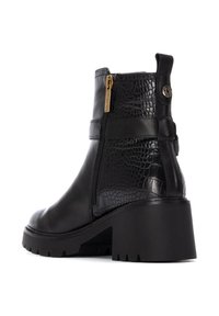 Botas de tobillo de cuero negro con un patrón de cocodrilo texturizado, cierre de cremallera y un tacón grueso. Suela robusta con detalles muesca.