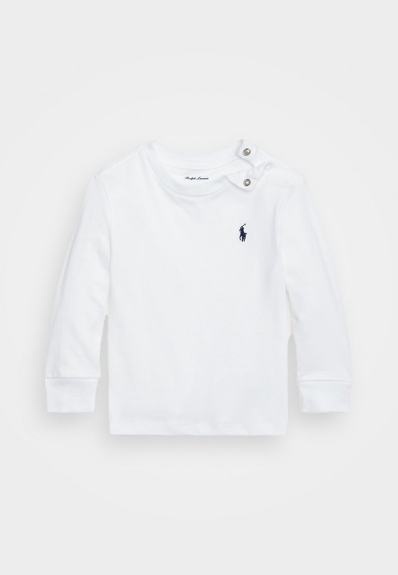 Vit långärmad skjorta i bomull med två silverknappar på vänster axel och en marinblå logotyp på vänster bröst.