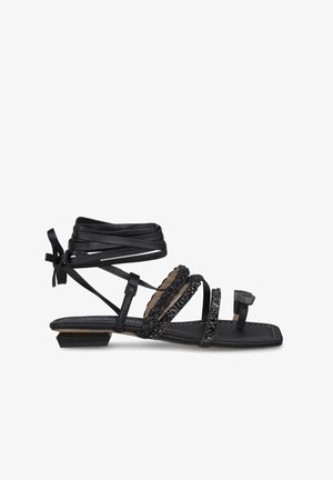 Black sandal with multiple straps, beaded accents, and a flat heel. Designed with ankle ties and a decorative buckle. Textured sole.