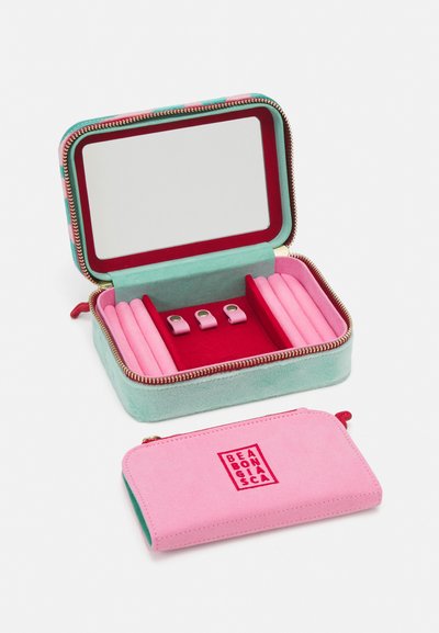 Smykkeskrin i teal og rosa semsket skinn, med speil, rød innredning og rom for ringer. Inkluderer en matchende rosa pose.