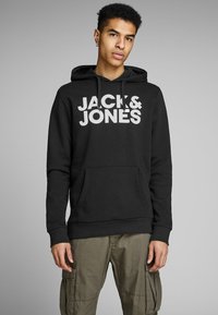 Black hooded sweatshirt with a front pocket and a large white printed logo, made from soft cotton material. Features drawstrings at the hood.