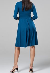 Turbulens klänning vid knäna med trekvartsärmar, figursydd överdel och utsvängd kjol; slät tyg; bärs med svarta stilettklackar.