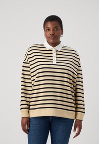 Beige och svart randig långärmad polo med vit krage, med knapplåsning och ribbade ärmslut, ihop med blå jeans.