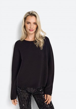 Black knit sweater with a round neckline, long sleeves, and a relaxed fit, paired with sequined black pants featuring vertical lines.