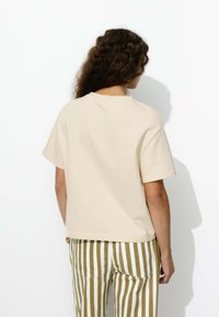 T-shirt en coton beige à manches courtes et à encolure ronde, associé à un pantalon à rayures verticales olive et blanches. Design simple, coupe décontractée.