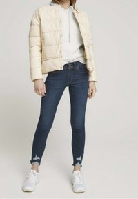 Fyllig off-white jacka med en kortad design, parat med mörkblå skinny jeans med slitna nederkant och vita sneakers.