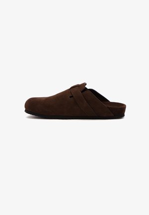 Brown suede slip-on shoe with a rounded toe, featuring a side strap detail and a textured black rubber sole.