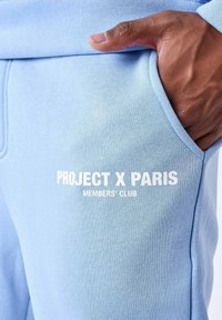 Lichtblauwe katoen joggers met een zijzak, met prominent gedrukte witte tekst "PROJECT X PARIS" en "MEMBERS' CLUB".