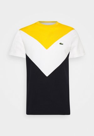 Kurzärmeliges T-Shirt mit gelbem Oberteil, weißem mittlerem Chevron, schwarzem Unterteil und kleinem grünen Krokodillogo auf der linken Brust.