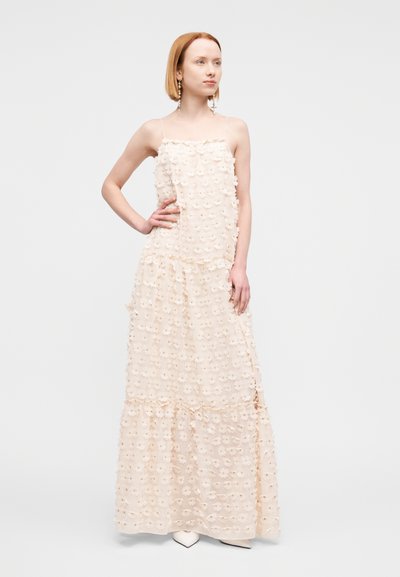 Robe longue en tissu léger et texturé avec des volants superposés, ornée d'appliqués floraux dans un doux beige. Bretelles spaghetti.