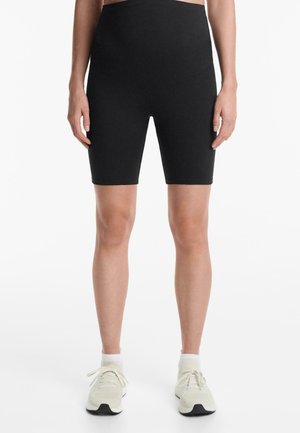 Shorts de vélo noirs taille haute en tissu extensible, offrant une texture lisse et une coupe ajustée, associés à des chaussures de sport légères.