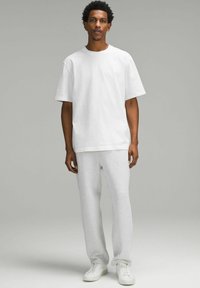 Vit bomulls t-shirt med lös passform, matchad med ljusgråa träningsbyxor och vita sneakers, stående mot en neutral bakgrund.