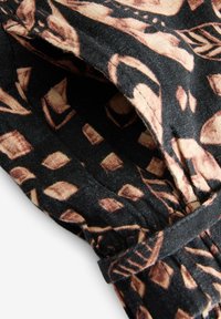 Tissu noir avec un motif géométrique marron de feuilles et de diamants, détail froncé et un lien ou passant en tissu assorti.