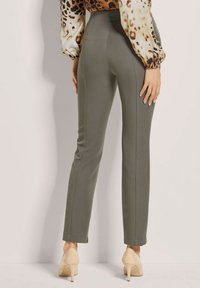 Op maat gemaakte olijfgroene broek met een gladde textuur, hoge taille en zijnaad. Gecombineerd met beige hoge hakken en een gebloemd blouse.