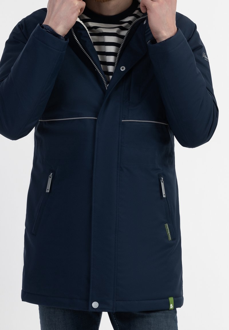 Navy blue winter coat with a zip and snap closure, featuring two side pockets, contrasting grey piping, and a green accent at the hem.