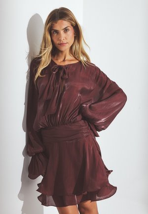 Maroon dress with a flowing silhouette, featuring a tied neckline, long voluminous sleeves, and layered ruffle hem detail. Smooth, lightweight fabric.