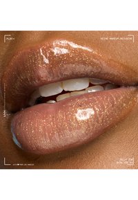 Lèvres brillantes avec un éclat doré et dents légèrement entrouvertes sur un ton de peau brun moyen, mettant en valeur un effet gloss scintillant.