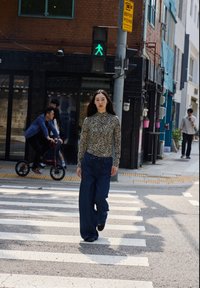 Top a maniche lunghe con motivo zebra abbinato a pantaloni jeans blu larghi e comodi. Strisce pedonali in un ambiente cittadino con persone e semafori.