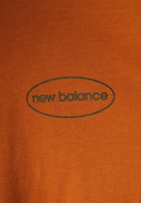 Oranje katoenen T-shirt met een donkergroen "new balance" logo in een ovale vorm in het midden. Gladde textuur met geribd stof.