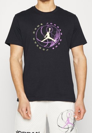 Homme portant un T-shirt Jordan noir avec un graphisme de basket-ball violet et jaune et un short blanc avec le logo Jordan assorti et un design basket-ball.