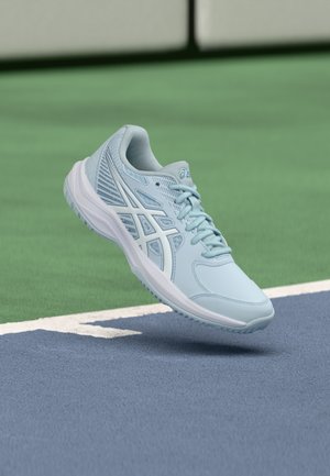 Zapatilla deportiva azul clara con parte superior de malla, detalles texturizados y suela acolchada, suspendida sobre una superficie de cancha azul.