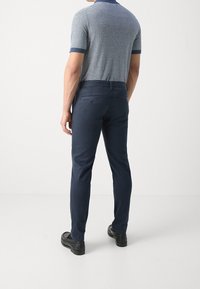 Pantaloni blu navy con una texture liscia, modello slim fit e due tasche posteriori. Abbinati a una polo a righe con colletto scuro.