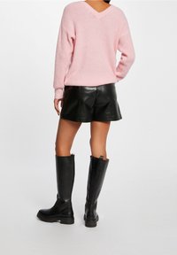 Pull en maille rose clair avec un col en V, associé à un short en cuir noir et des bottes noires montant jusqu''aux genoux, présentant une texture lisse et une coupe ajustée.