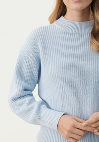 Vaaleansininen neulepusero, jossa on korkea kaulus, ribbireunat ja teksturoitu kuvio. Ominaisuuksiin kuuluu rento istuvuus ja pehmeä kangas.