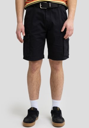 Zwarte cargoshorts met zijzakken, gemaakt van katoen. Bevat een riem en wordt gedragen met zwarte sneakers en witte sokken.