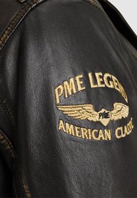 Crna kožna jakna s izvezenim logotipom "PME Legend" i "American Classic" u zlatnoj boji, s naglašenim detaljnim šavovima.