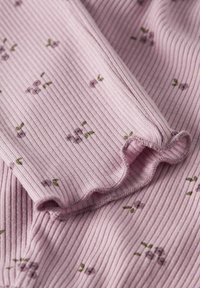 Roze ribstof met kleine bloempatronen in paars en groen. De stof heeft een gerimpelde rand langs de manchet.