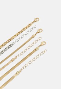 Cinq chaînes métalliques exposées : deux en or, une en argent, une texturée et une avec des maillons. Elles sont toutes équipées de fermoirs à mousqueton pour attacher.